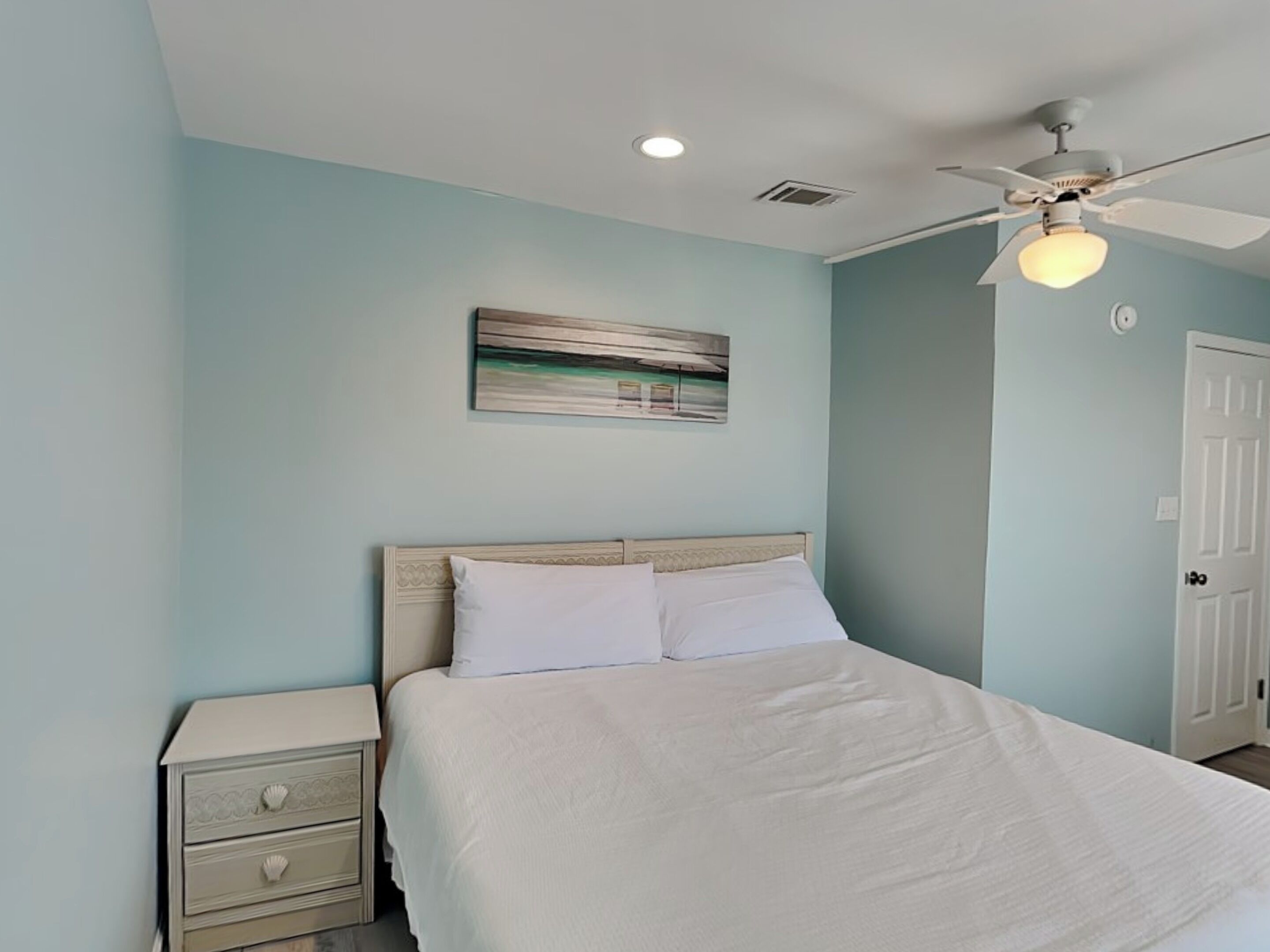 A bedroom with a bed, a nightstand, a ceiling fan, and a door.