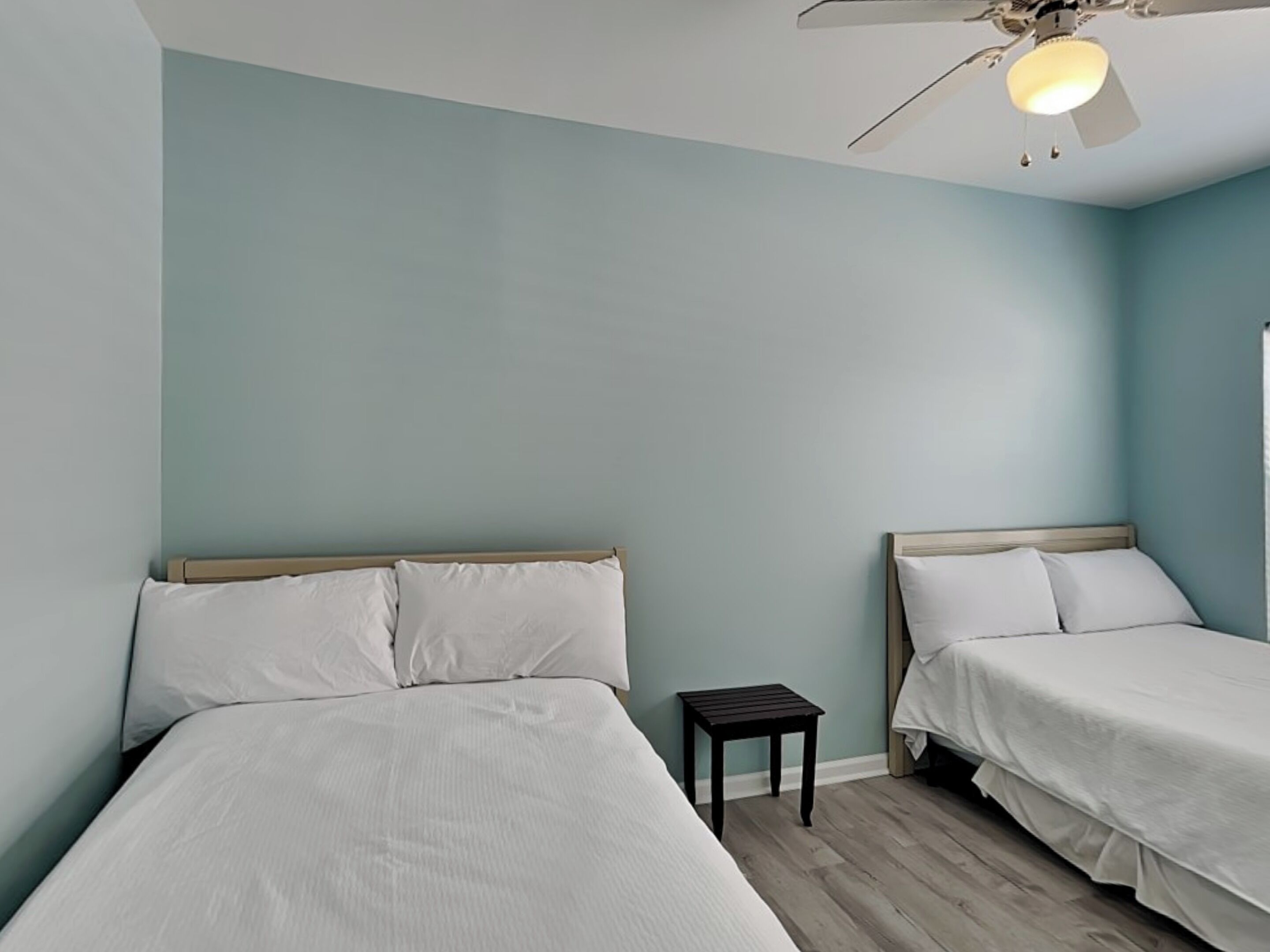 A room with two beds, a small table, and a ceiling fan.