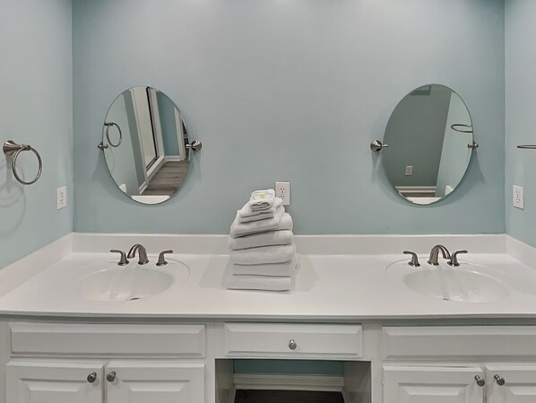 A bathroom with two sinks, two mirrors, and a stack of white towels on the counter.