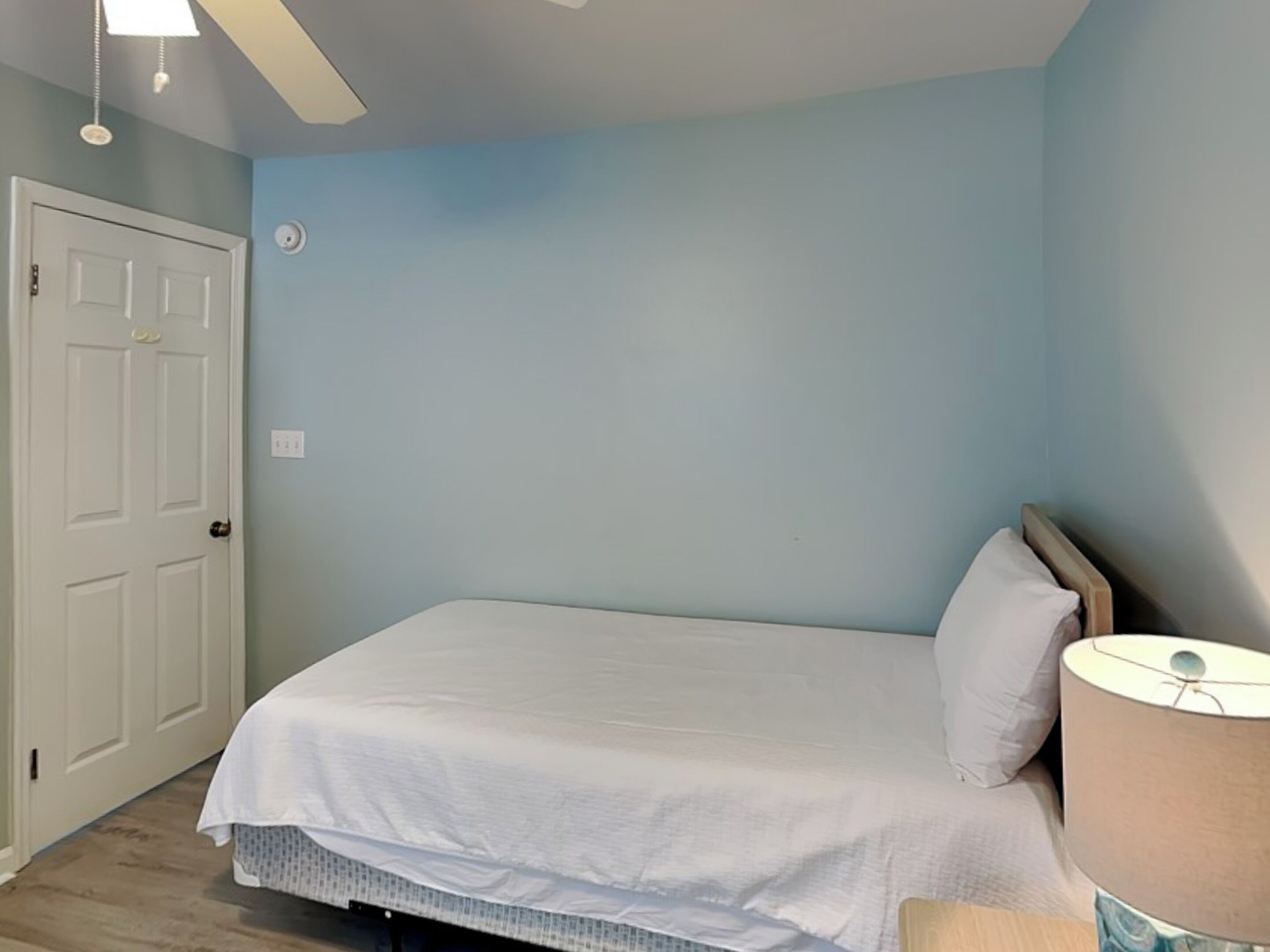 A bedroom with a bed, a nightstand, a lamp, and a door.