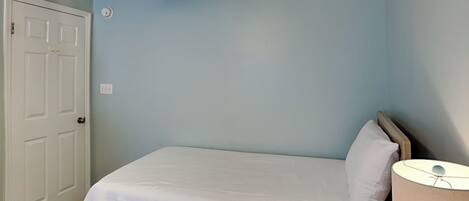 A bedroom with a bed, a nightstand, a lamp, and a door.