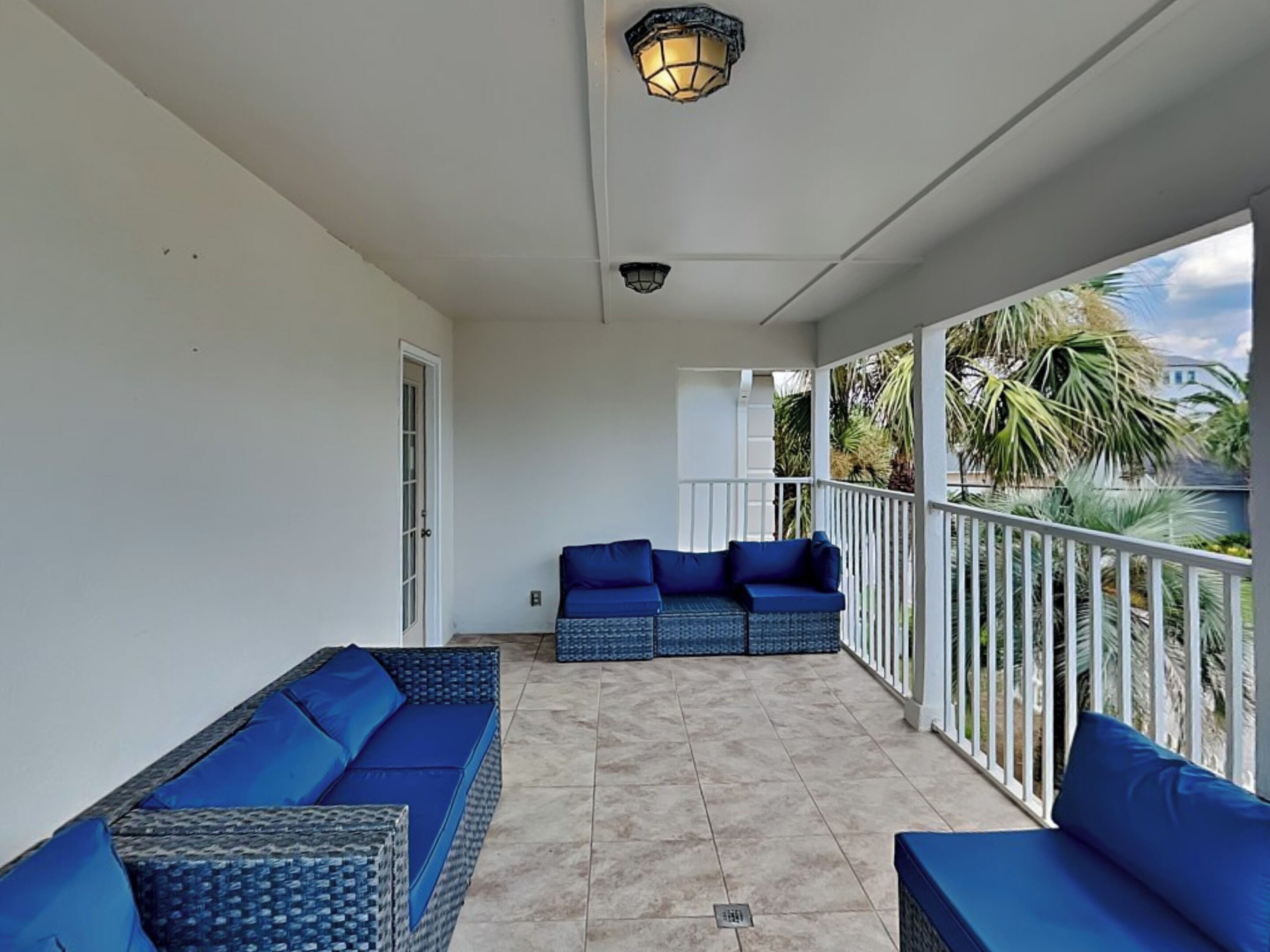 A covered balcony with wicker furniture and a view of palm trees.