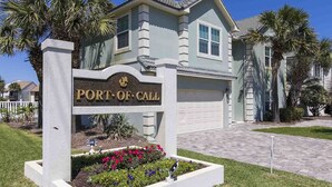 Ein Wohnhaus mit einem Schild, auf dem 'PORT OF CALL' steht, und einem gepflegten Vorgarten mit bunten Blumen.