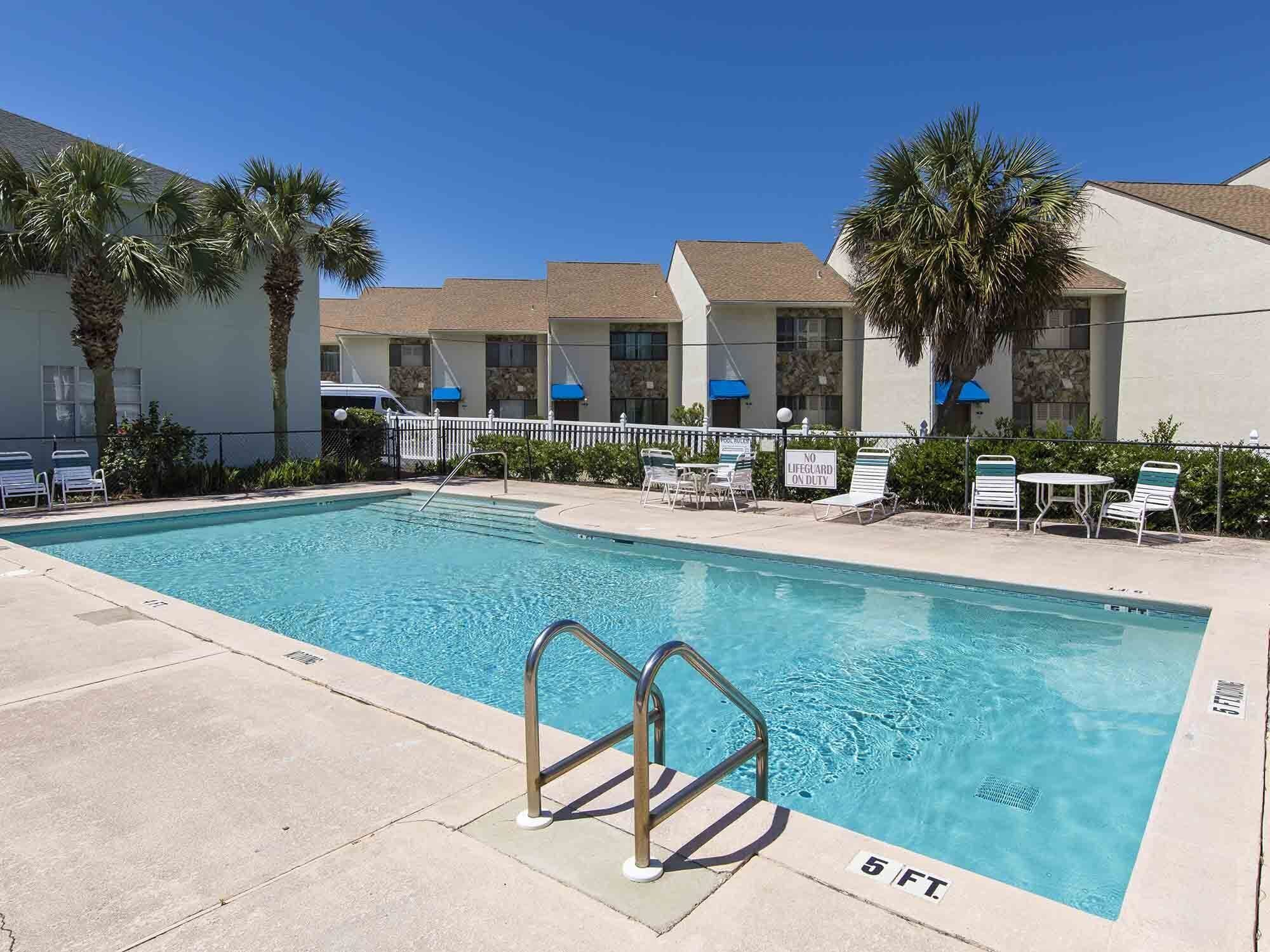 A swimming pool with a lifeguard sign, lounge chairs, and palm trees.