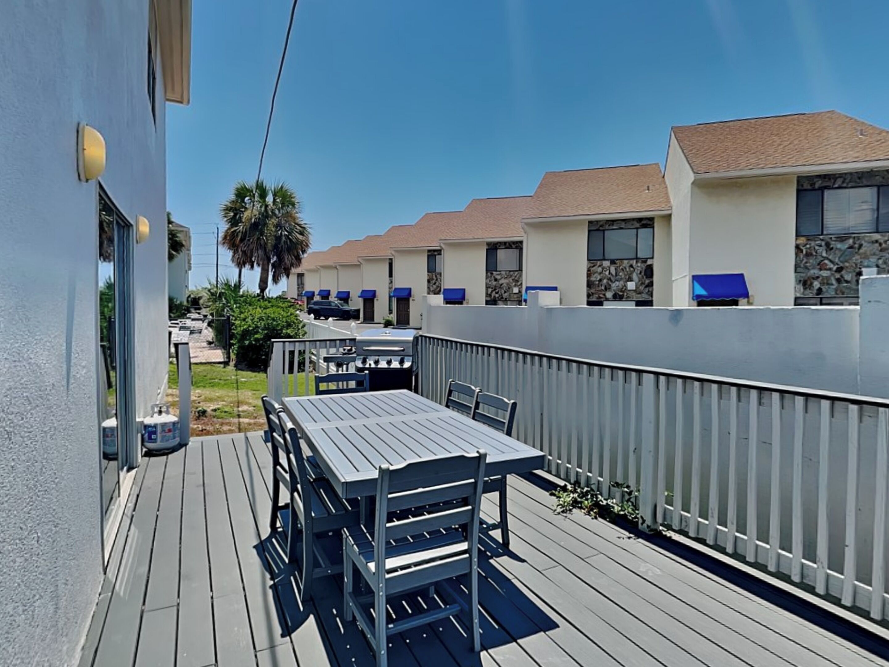 A deck with a table and chairs, a grill, and a white fence.