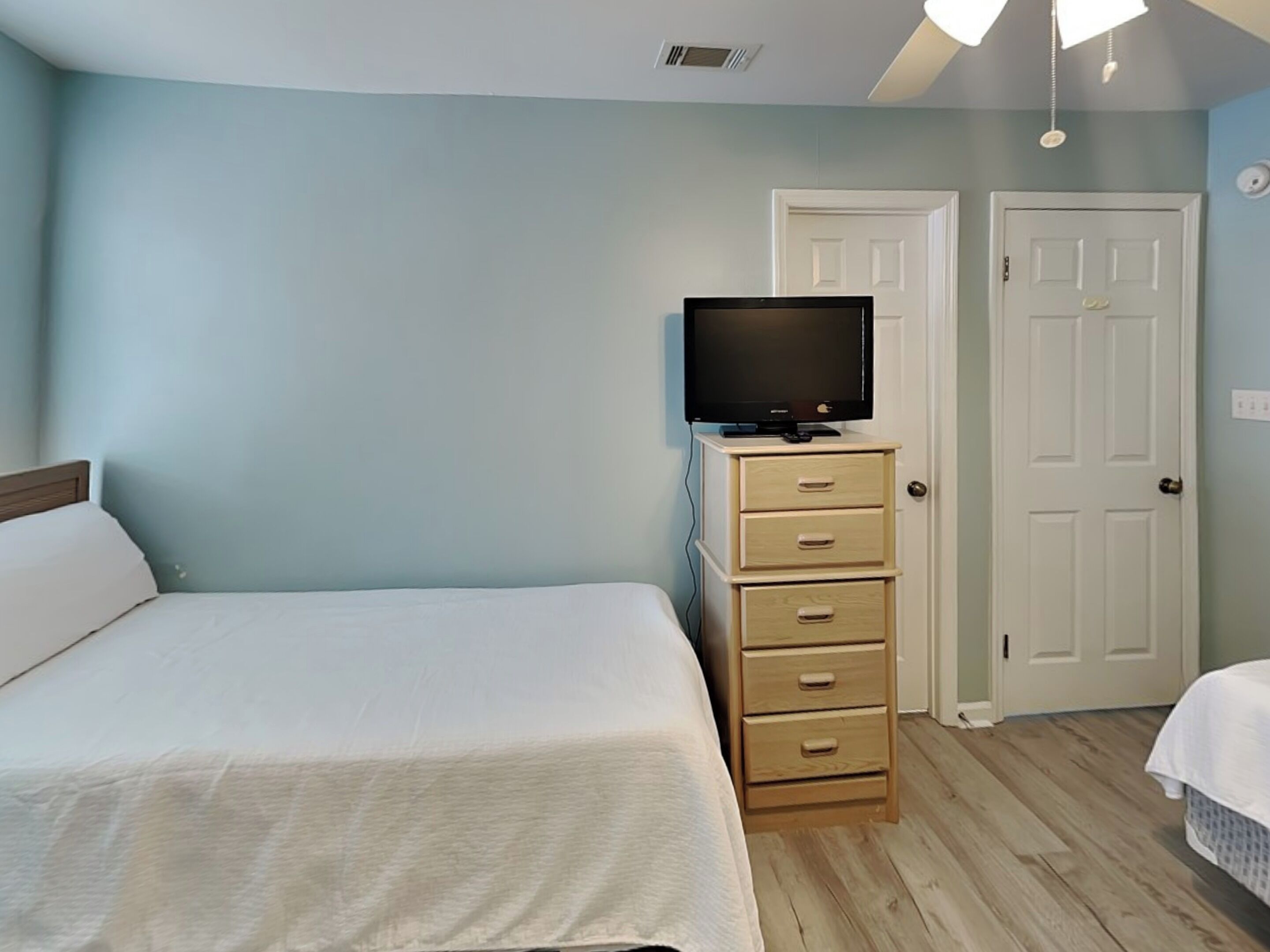 A bedroom with a bed, a television on a dresser, a door, and a light fixture.