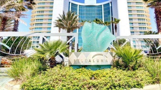 A hotel with a modern design, featuring a central glass facade and a distinctive turquoise sculpture in front. - Bella Luna #404 by Southern Vacation Rentals (Orange Beach)