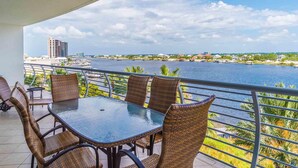 A balcony with wicker chairs and a glass table overlooking a river with buildings in the background. - Bella Luna #404 by Southern Vacation Rentals (Orange Beach)
