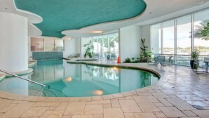 An indoor swimming pool with a curved ceiling, large windows, and a view of the cityscape. - Bella Luna #404 by Southern Vacation Rentals (Orange Beach)