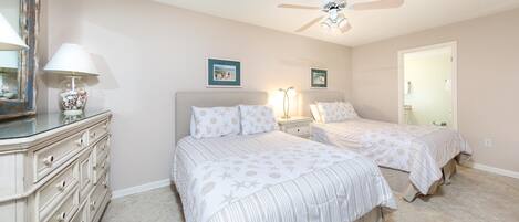 A bedroom with two beds, a dresser, a ceiling fan, and a door leading to another room.