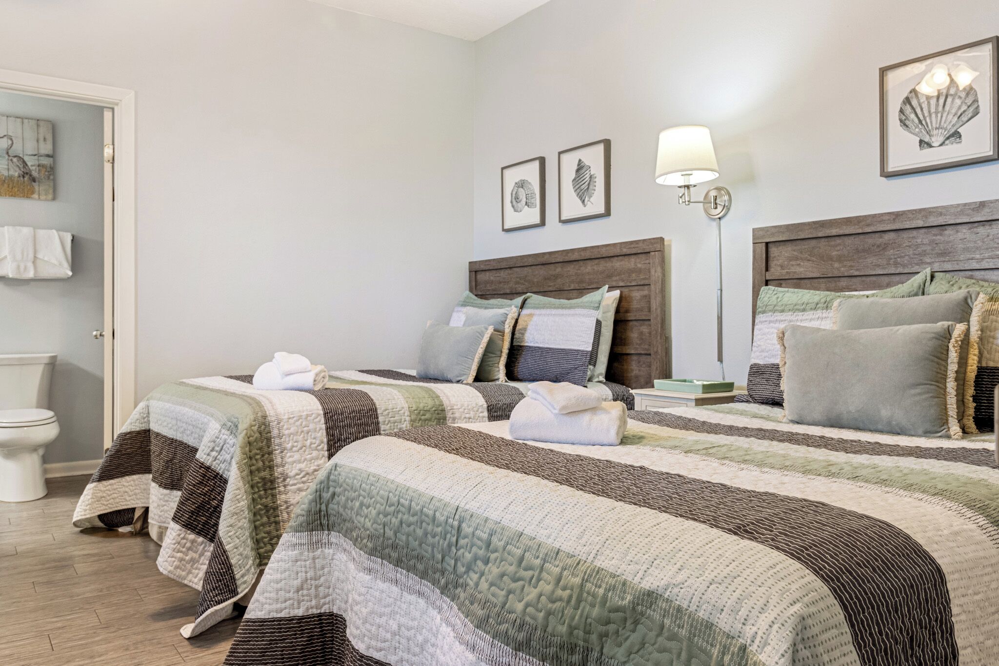 A hotel room with two beds, a wooden headboard, a wall-mounted lamp, and framed artwork.