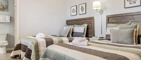 A hotel room with two beds, a wooden headboard, a wall-mounted lamp, and framed artwork.