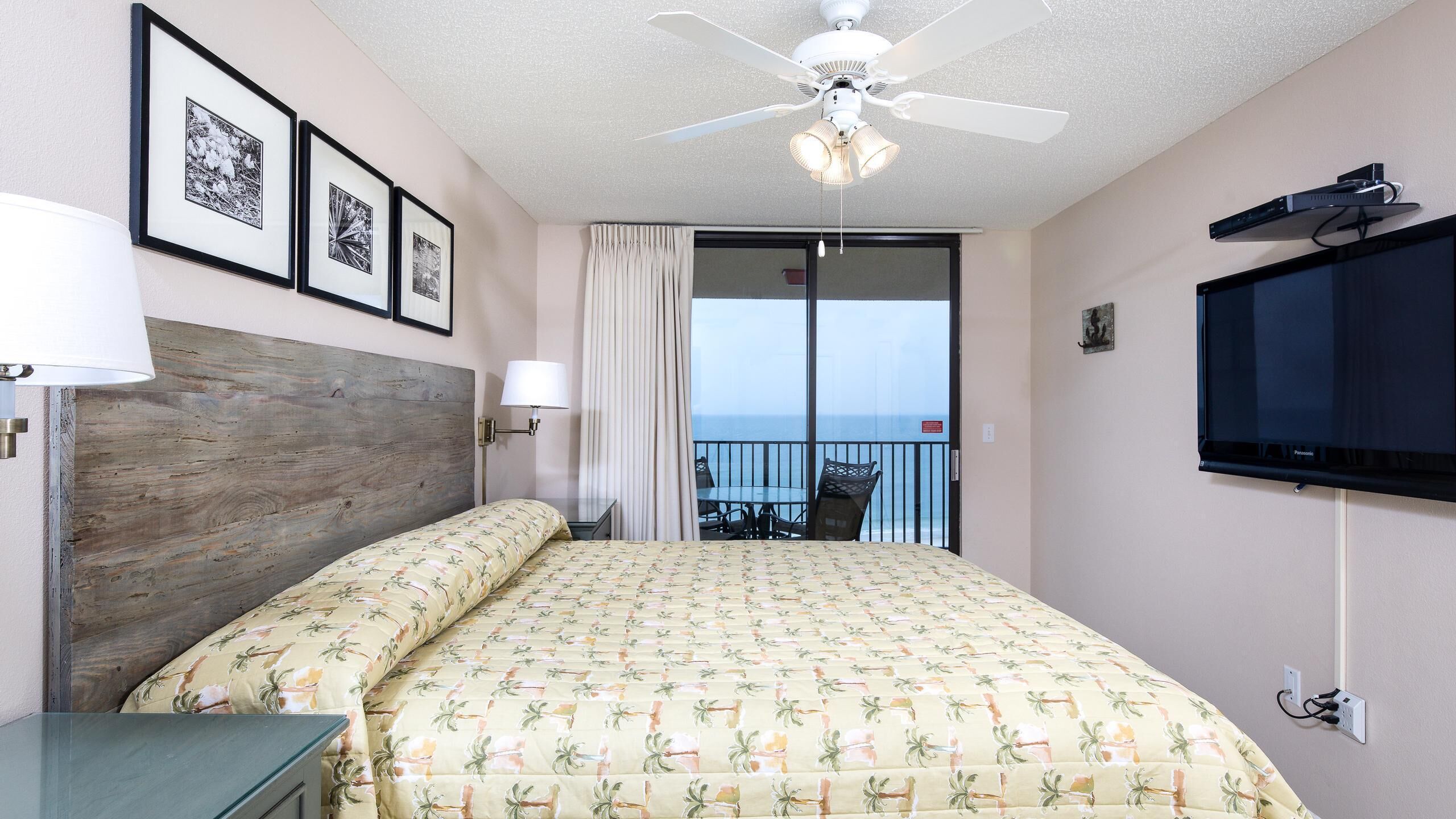 A hotel room with a bed, a ceiling fan, a TV, and a balcony with a view.
