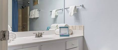 A bathroom with a white sink, a mirror, and a towel rack with multiple towels.