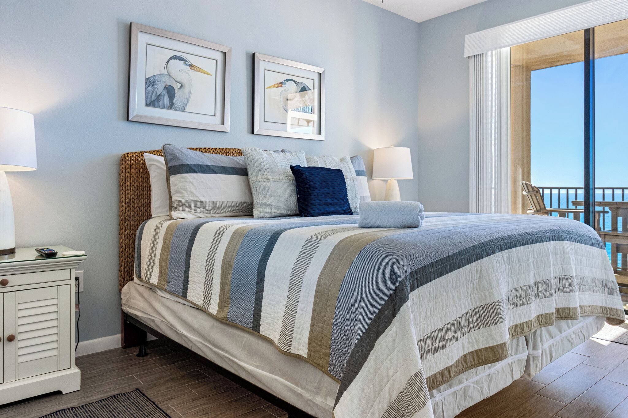 Une chambre à coucher comprenant un lit, deux tables de chevet, une commode, une fenêtre avec vue et deux œuvres d’art encadrées accrochées au mur.