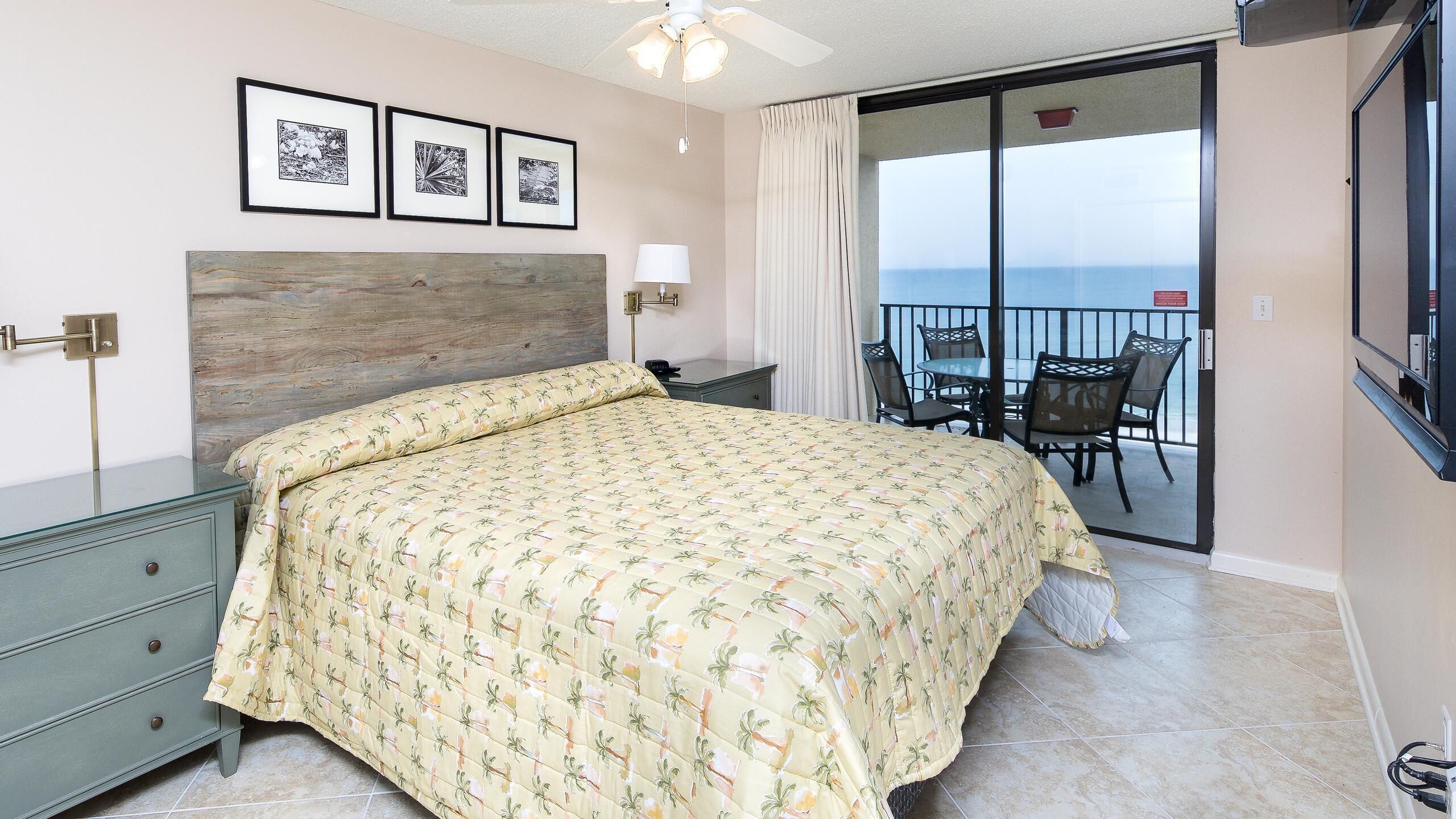 A bedroom with a bed, a nightstand, a lamp, and a view of the balcony.