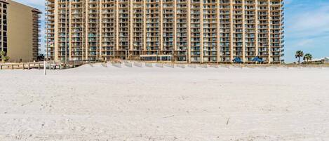 A high-rise hotel with multiple balconies, located adjacent to a sandy beach.