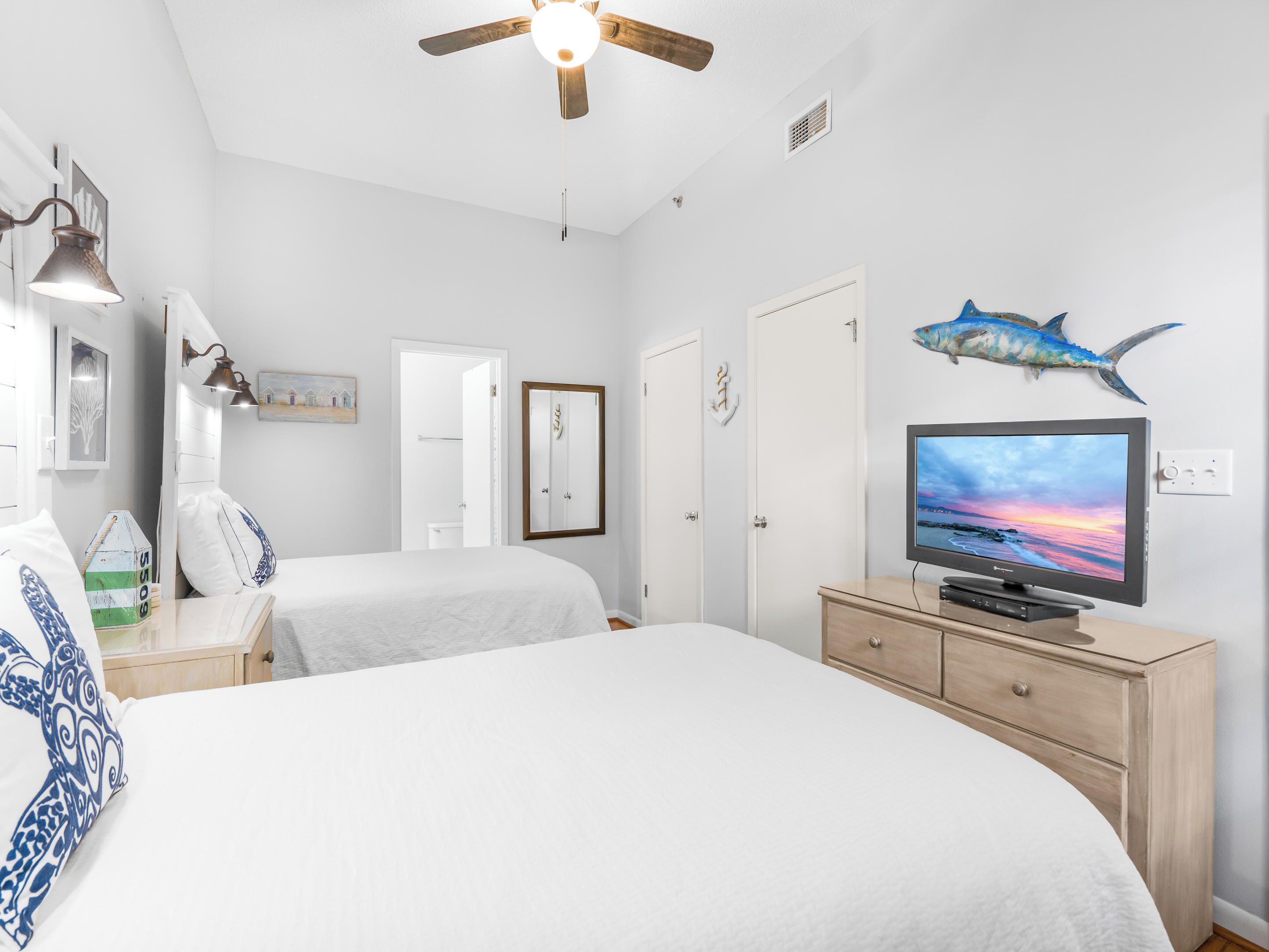A bedroom with two beds, a ceiling fan, a TV, and a decorative fish on the wall.
