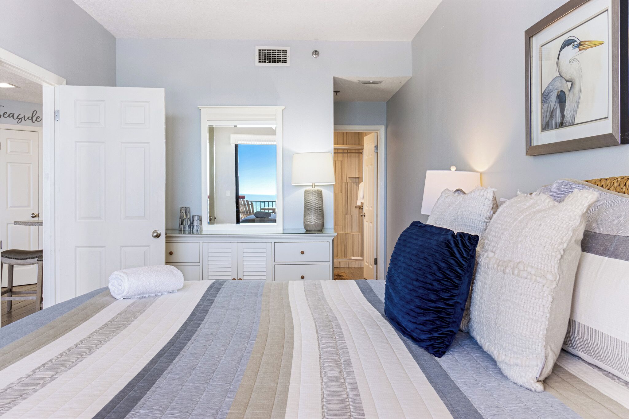 Une chambre à coucher avec un grand lit, une commode, un miroir et une œuvre d’art encadrée accrochée au mur.