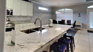 Una cocina moderna con armarios blancos, una isla grande con taburetes de bar y una ventana con persianas.