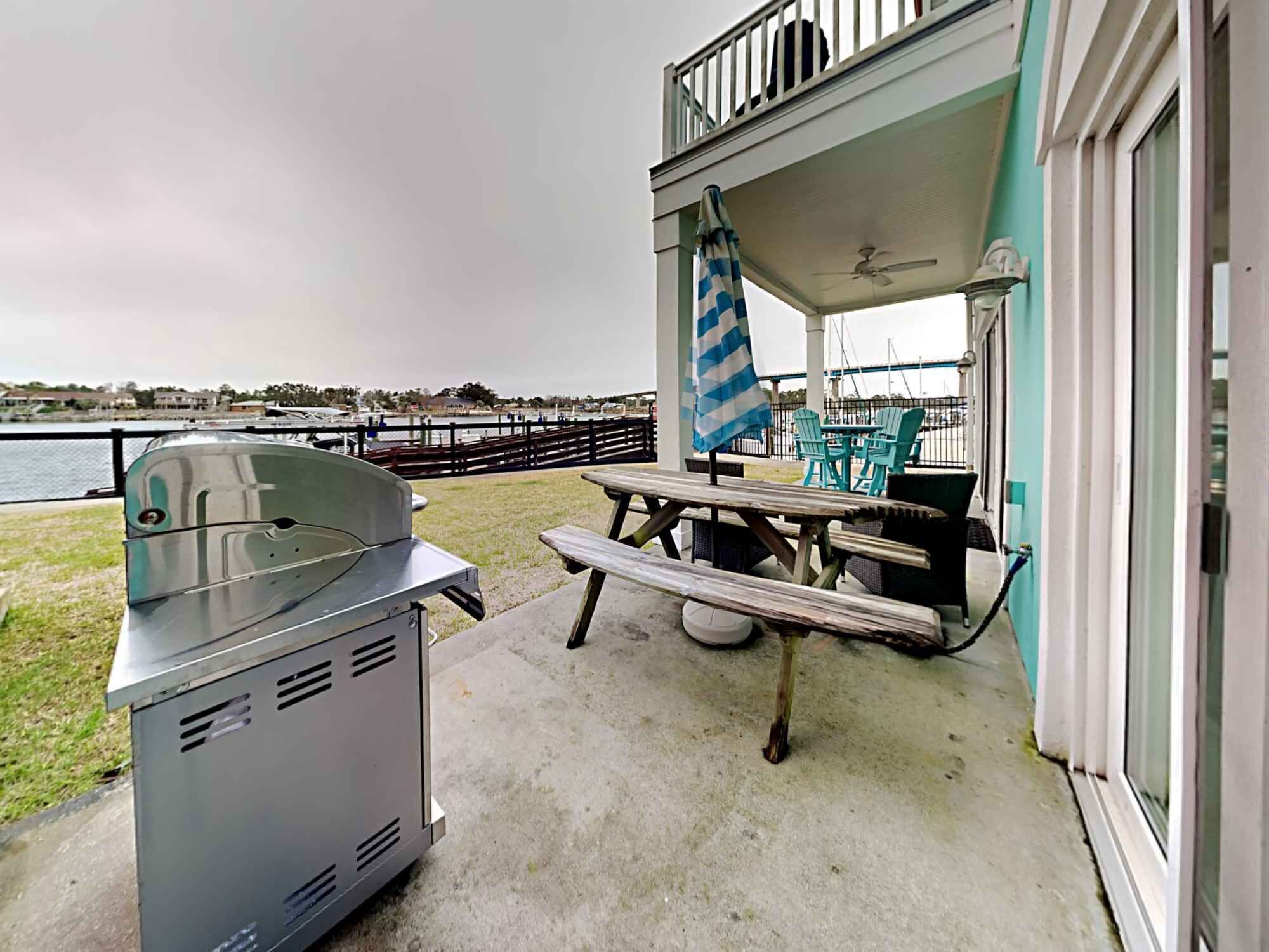 Un espace extérieur abrité, équipé d’un barbecue, d’une table de pique-nique et de chaises, et offrant une vue sur un plan d’eau.