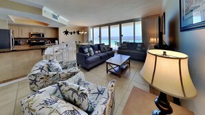 A modern living room with a sofa, armchairs, and a coffee table. There is a kitchen area with a refrigerator, oven, and microwave. The room has large windows offering a view of the sea. - Silver Shells St. Maarten #1405 by Southern Vacation Rentals (Destin)
