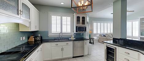 A modern kitchen with white cabinets, a black countertop, and a central island. There is a microwave, sink, and stainless steel appliances.