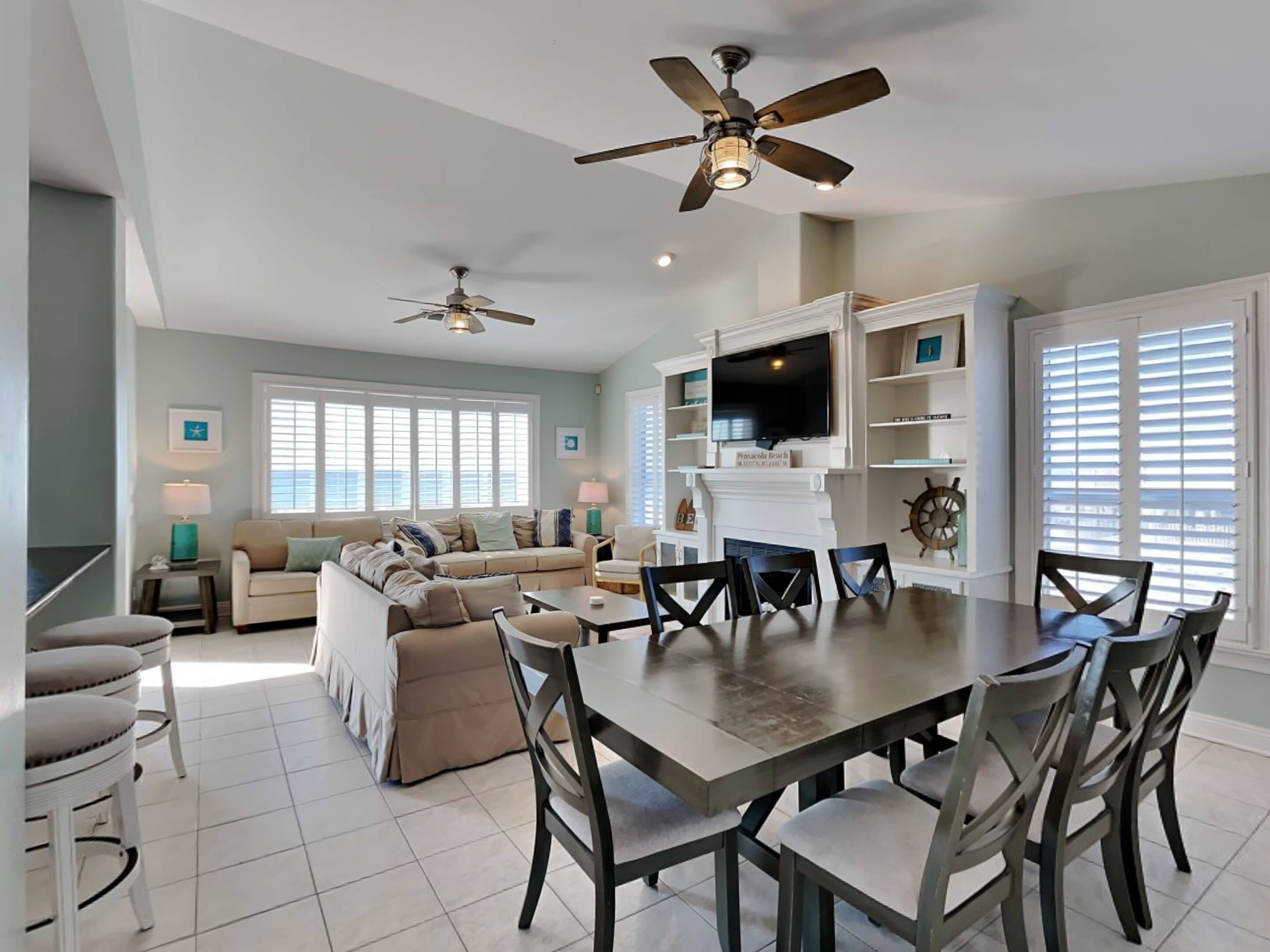 A spacious living room with a large dining table, two ceiling fans, and a fireplace.