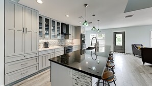 Une cuisine moderne dotée d’un grand îlot central, de meubles de rangement gris et d’un plan de travail noir.