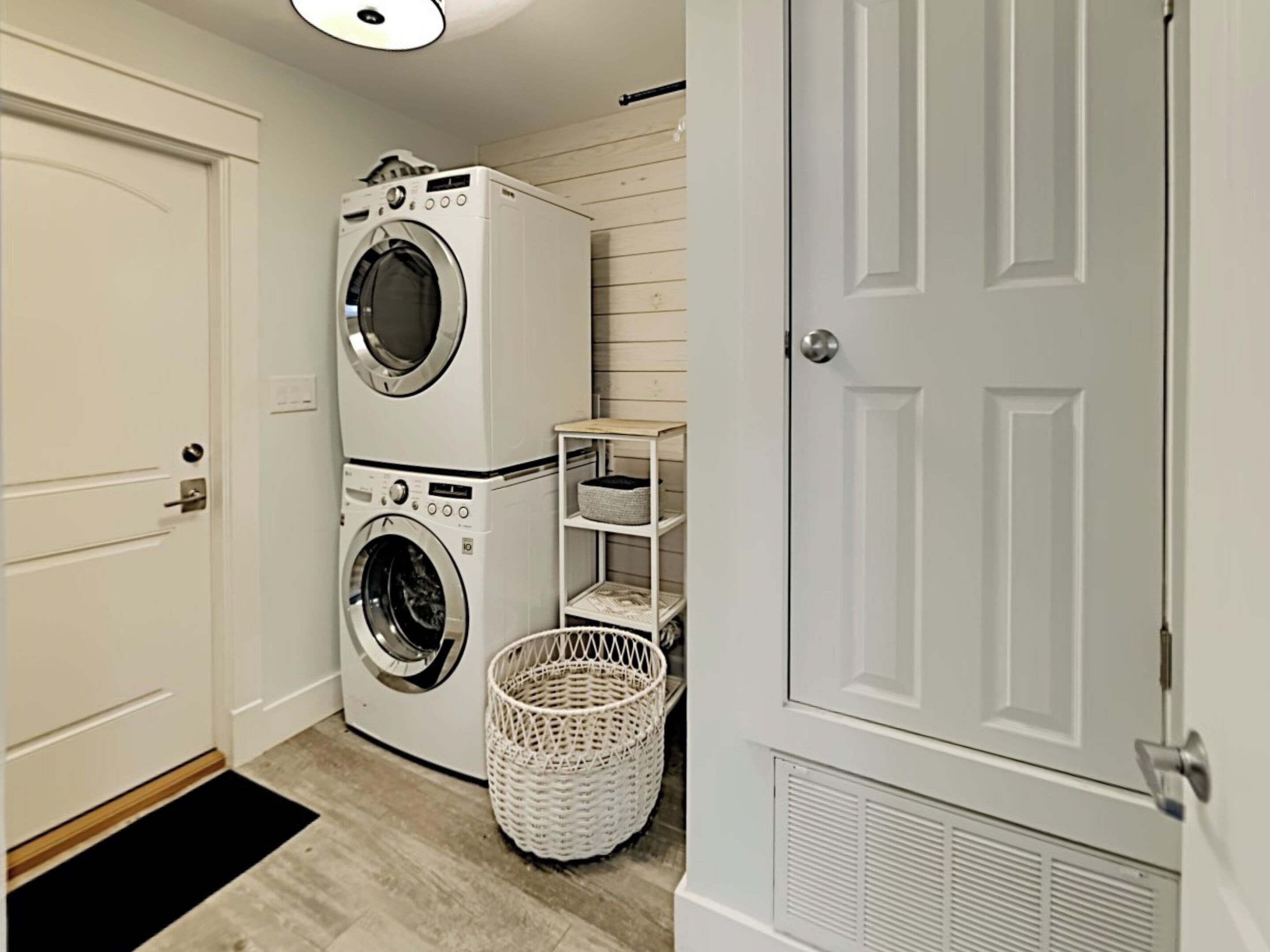 A laundry room with stacked washers and dryers, a basket, and a shelf with baskets.