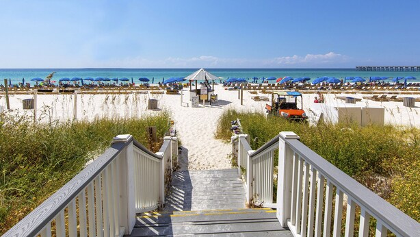A beach with a wooden staircase leading to a gazebo, surrounded by beach umbrellas and lounge chairs. - Calypso Resort & Towers #1809W by Resort Collection (Panama City Beach)