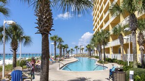 A resort pool area with palm trees, lounge chairs, and a view of the ocean. - Calypso Resort & Towers #1809W by Resort Collection (Panama City Beach)