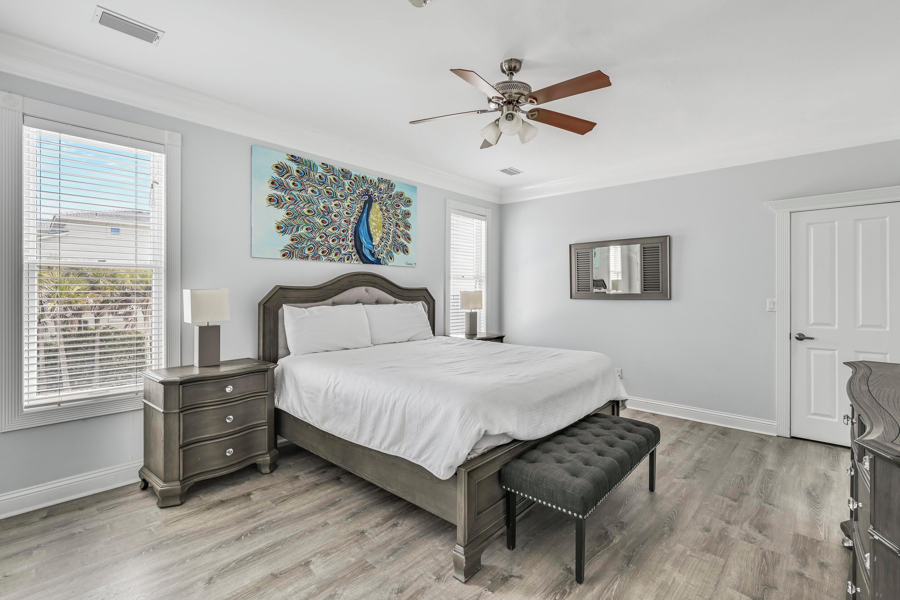 A bedroom with a bed, a nightstand, a bench, a ceiling fan, and a painting.