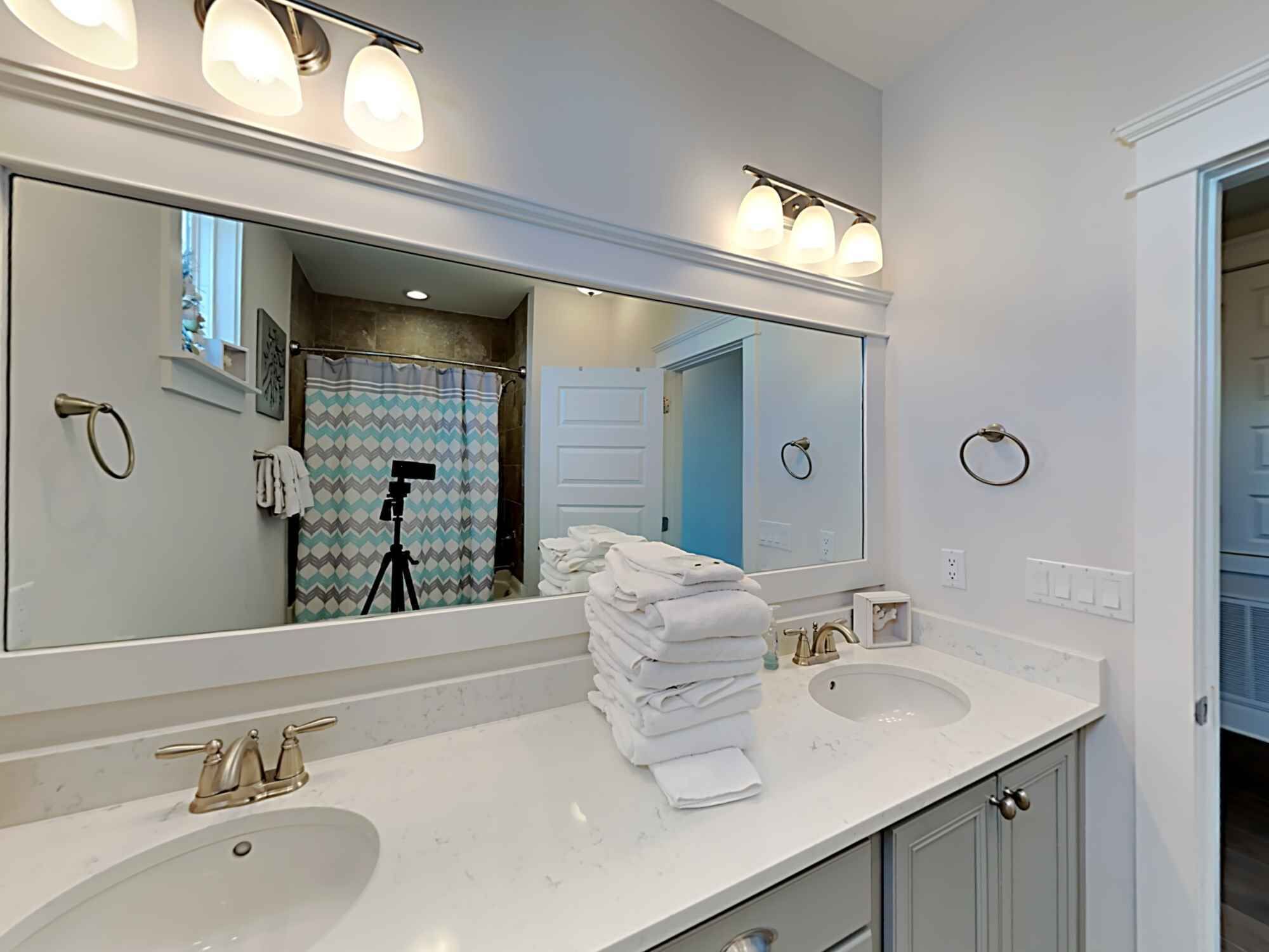 A bathroom with two sinks, a large mirror, and a shower curtain with a camera on it.
