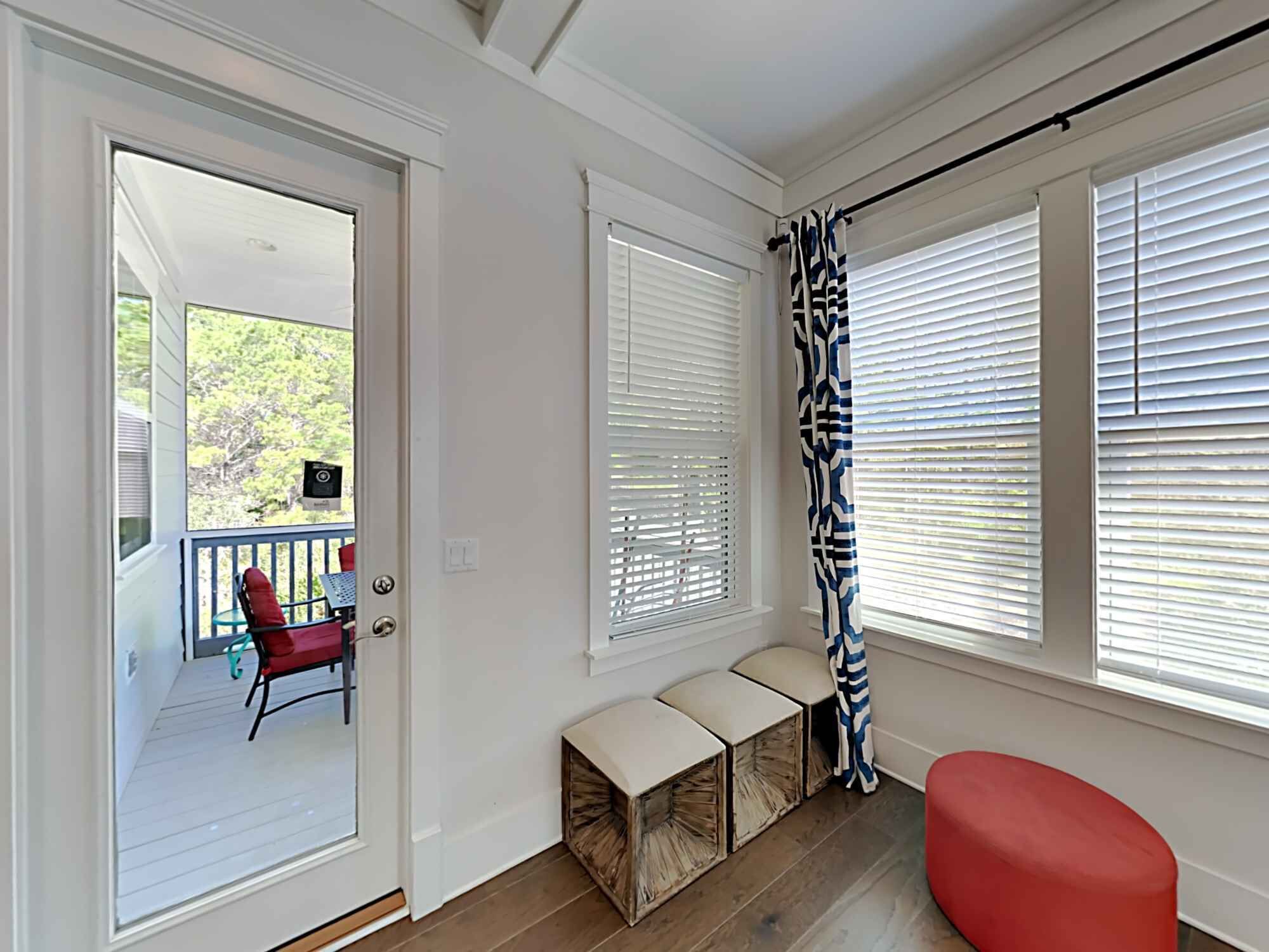 A room with a door leading to a balcony, a red chair, and a bench with storage boxes.
