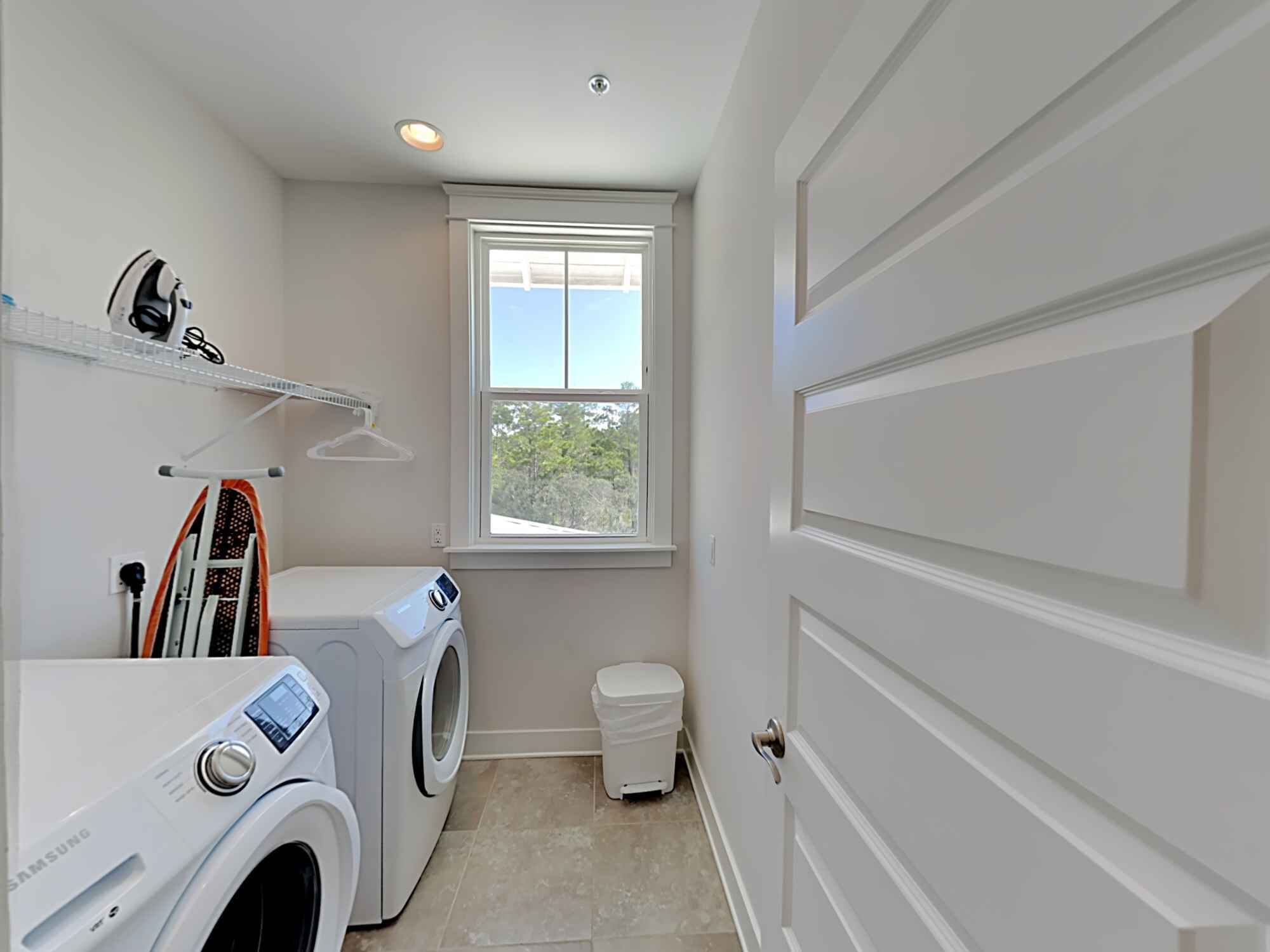 A compact laundry room with a washing machine, dryer, and a small trash bin.