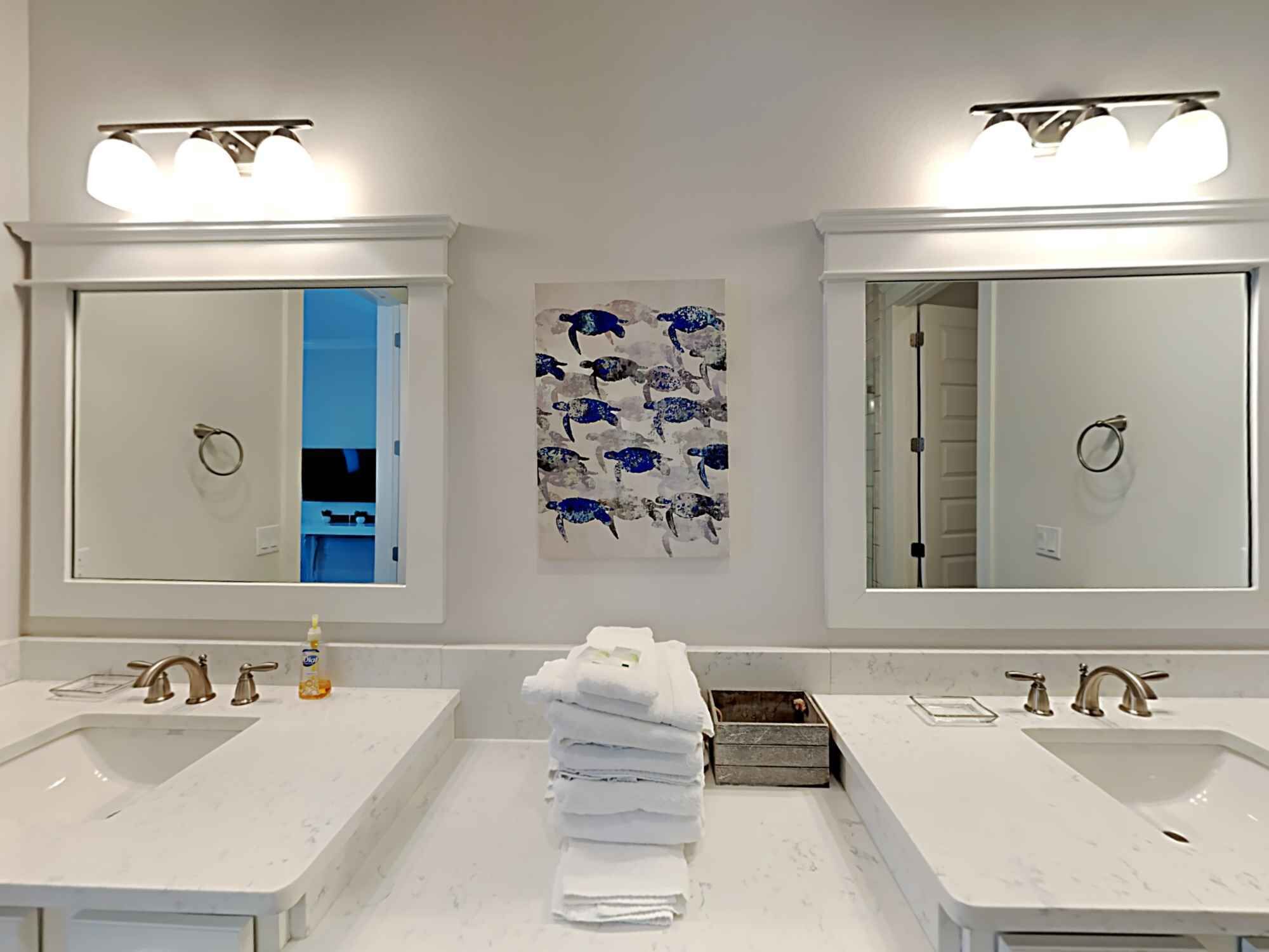 A bathroom with two sinks, a towel rack, and a wall-mounted artwork of sea turtles.