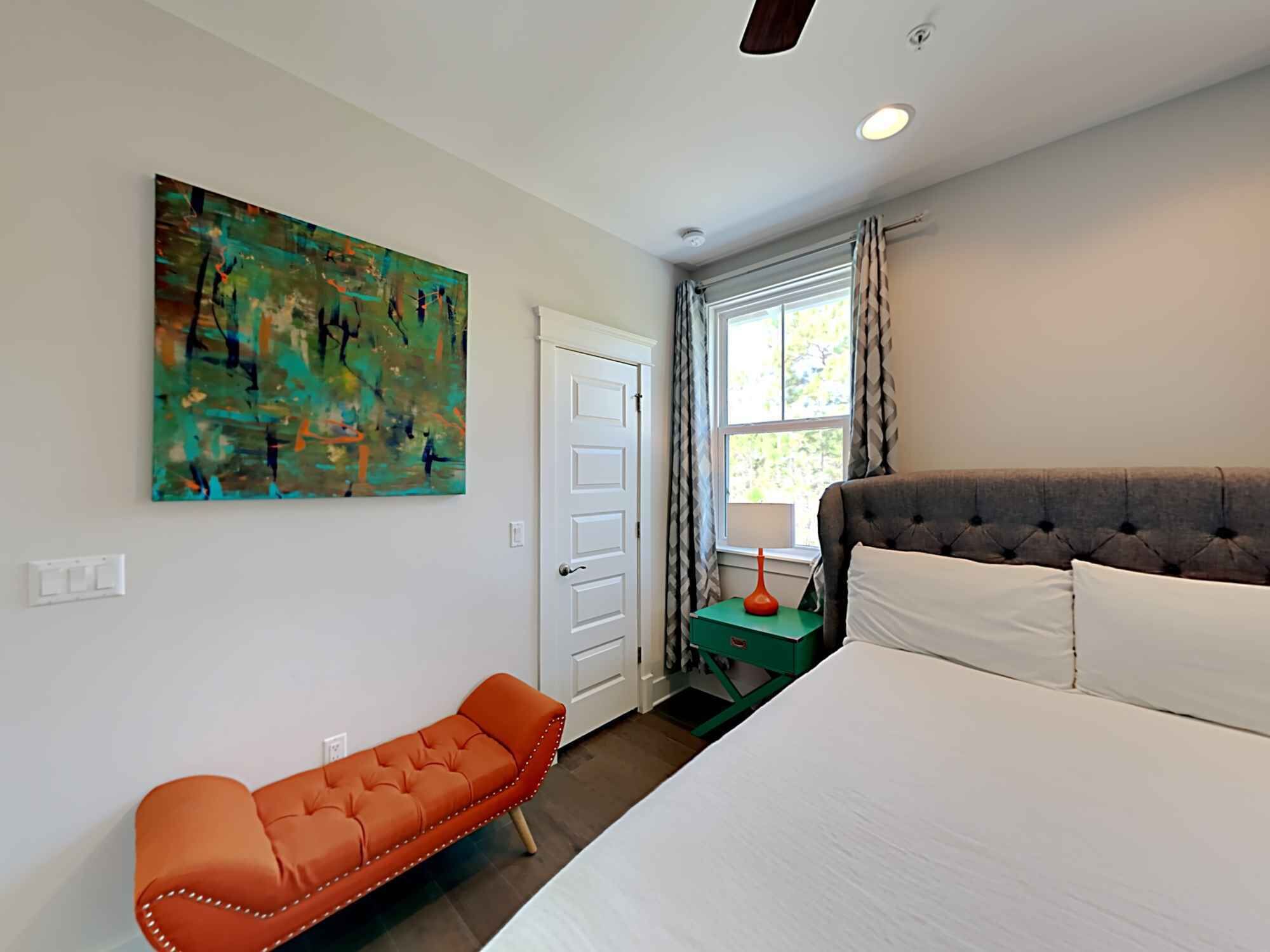 A bedroom with a bed, a chair, a painting, a window, and a door.
