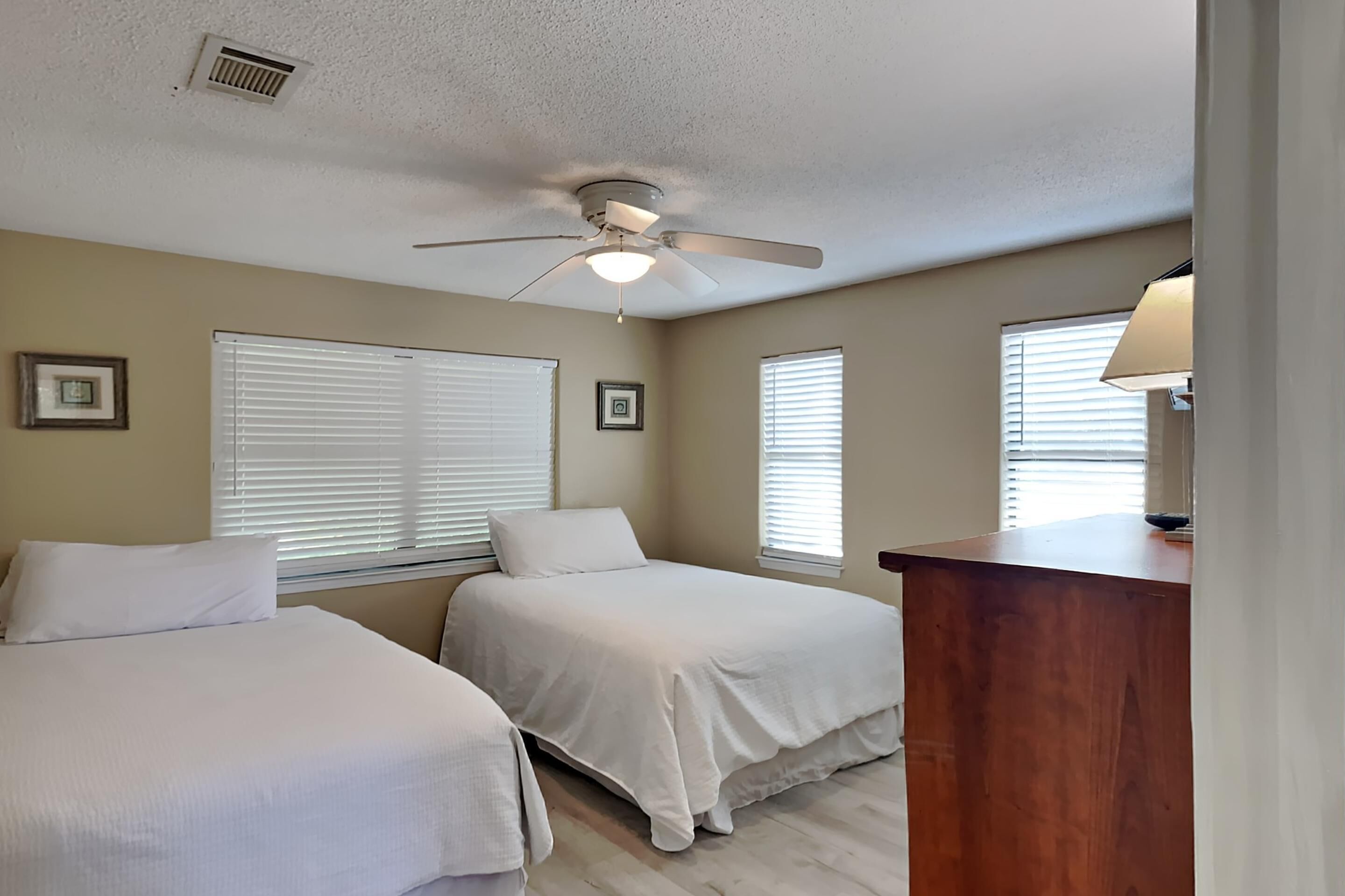 A bedroom with two beds, a ceiling fan, and a desk with a lamp.