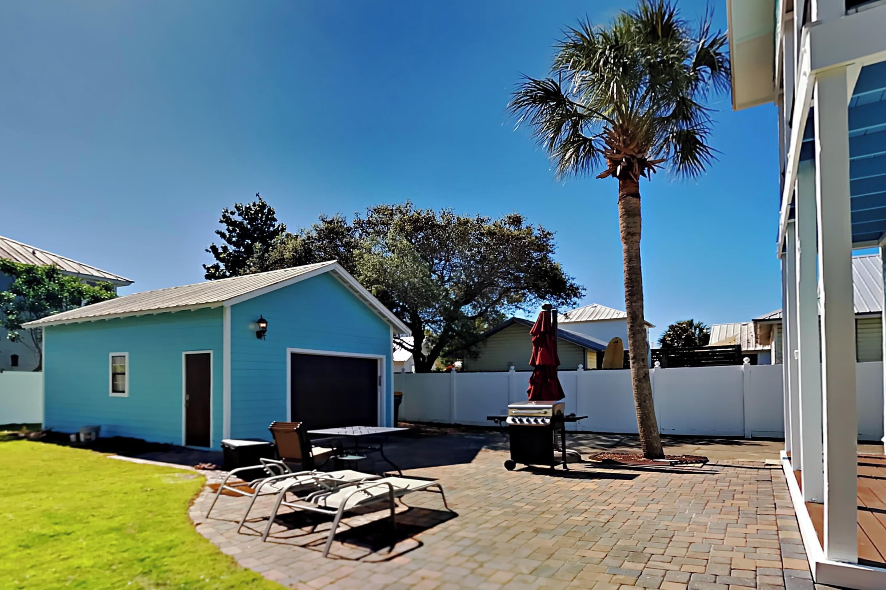 A backyard with a patio, a barbecue grill, a small shed, and a palm tree.