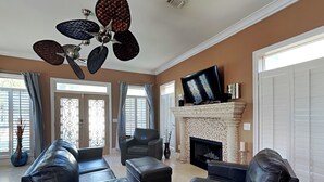 A spacious living room with a fireplace, leather sofas, a flat-screen TV, and a ceiling fan. - A Mid-Summer's Night Dream by Southern Vacation Rentals (Destin)
