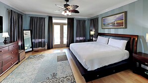 A hotel room with a large bed, a ceiling fan, a wooden dresser, a mirror, and a painting on the wall. - A Mid-Summer's Night Dream by Southern Vacation Rentals (Destin)