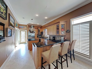 A modern kitchen with a central island, wooden cabinets, and a large window with blinds.