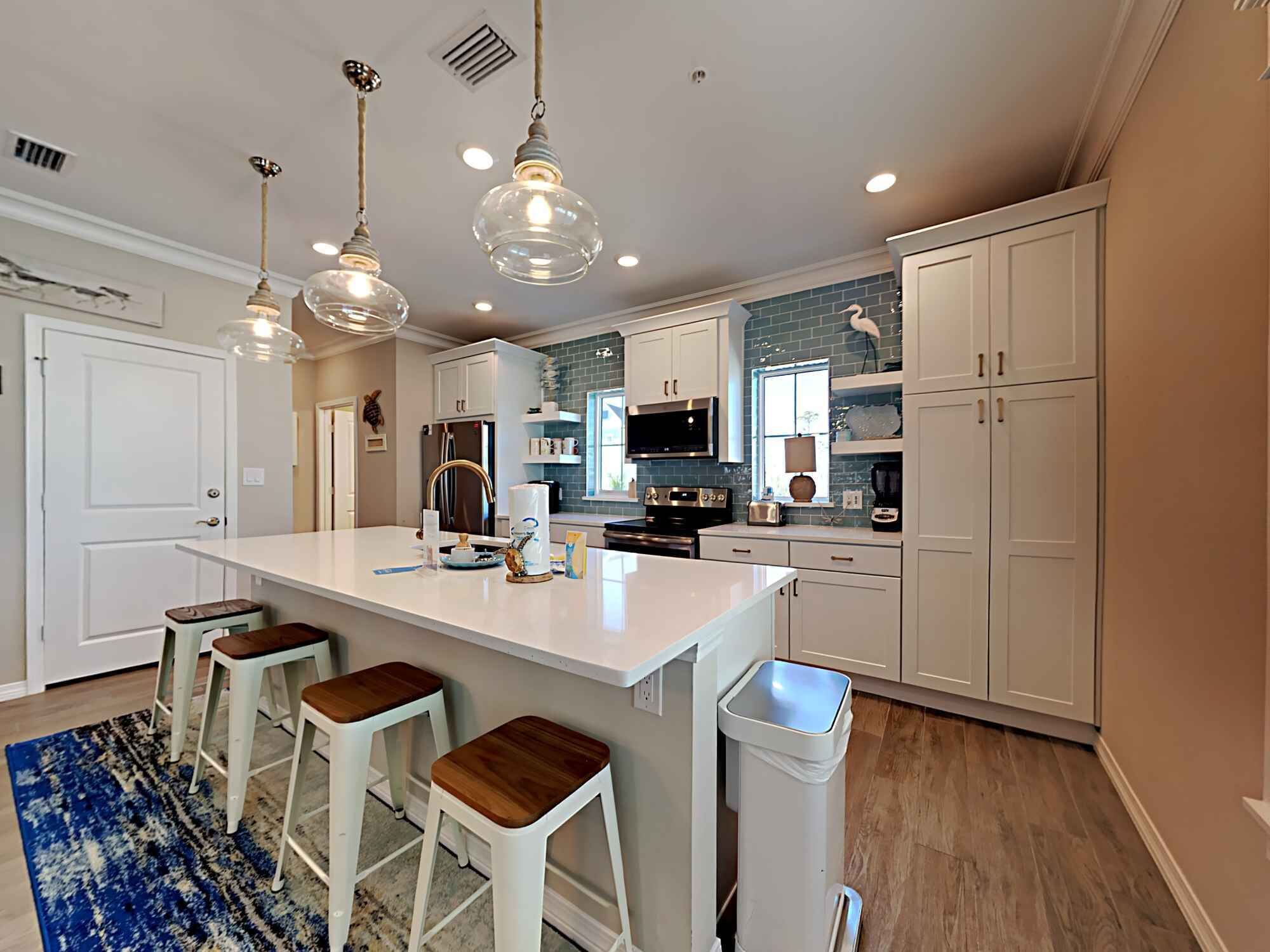 A modern kitchen with white cabinetry, a large island with stools, pendant lighting, and a blue accent wall.