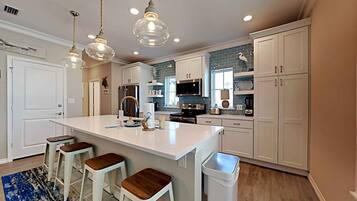 A modern kitchen with white cabinetry, a large island with stools, pendant lighting, and a blue accent wall.