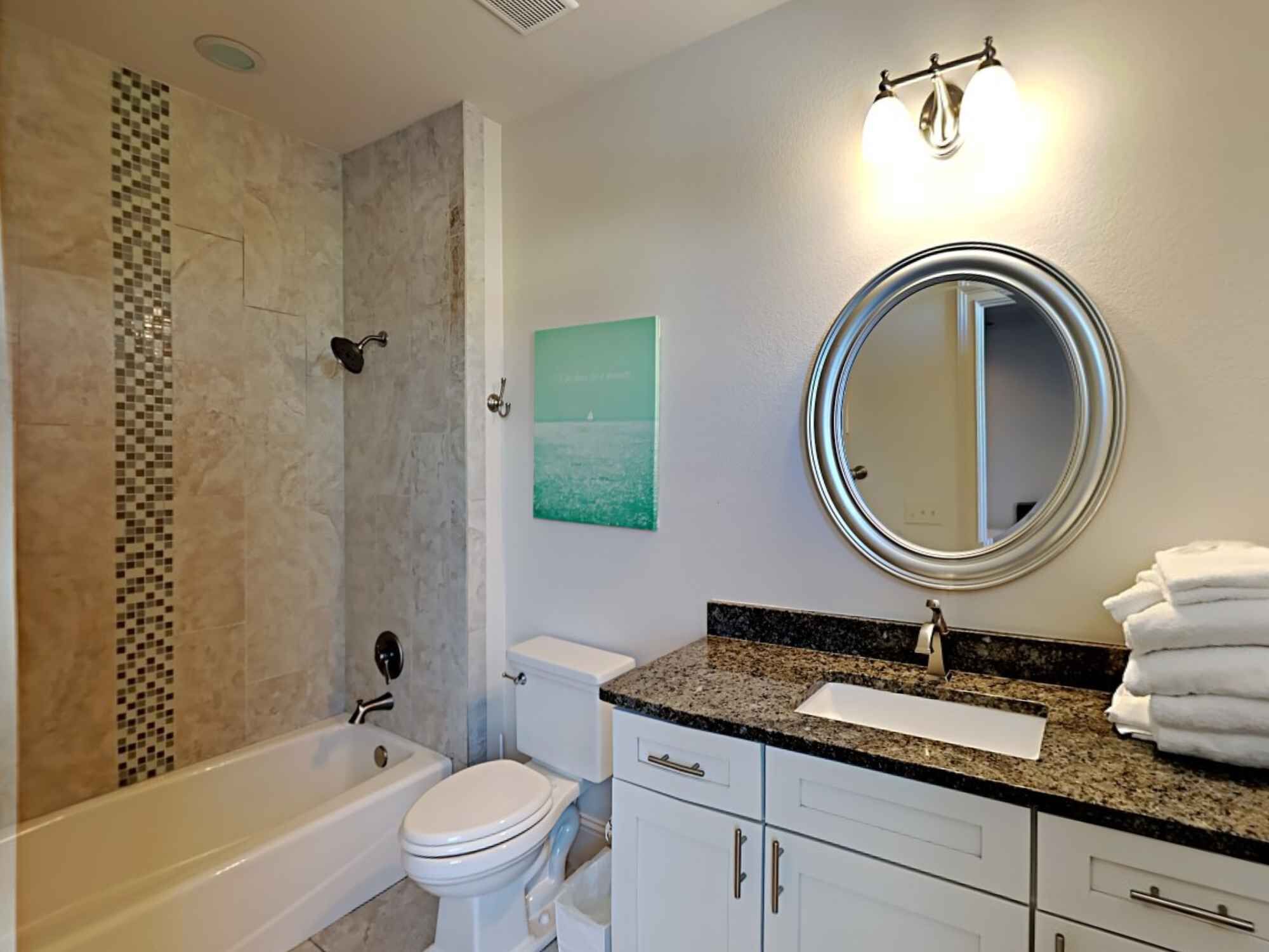 A bathroom with a bathtub, toilet, vanity with a sink, and a mirror.