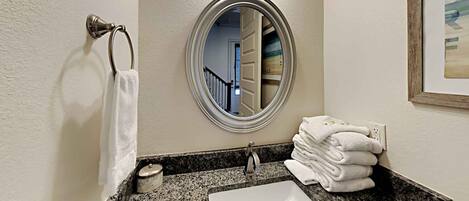A bathroom with a granite countertop, a white sink, a round mirror, and a towel rack with folded towels.