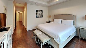 Hotellihuone, jossa on suuri sänky, kattotuuletin, yöpöytä lampun kanssa, penkki ja patteri.