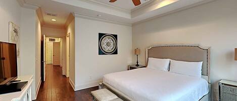 A hotel room with a large bed, a ceiling fan, a bedside table with a lamp, a bench, and a radiator.