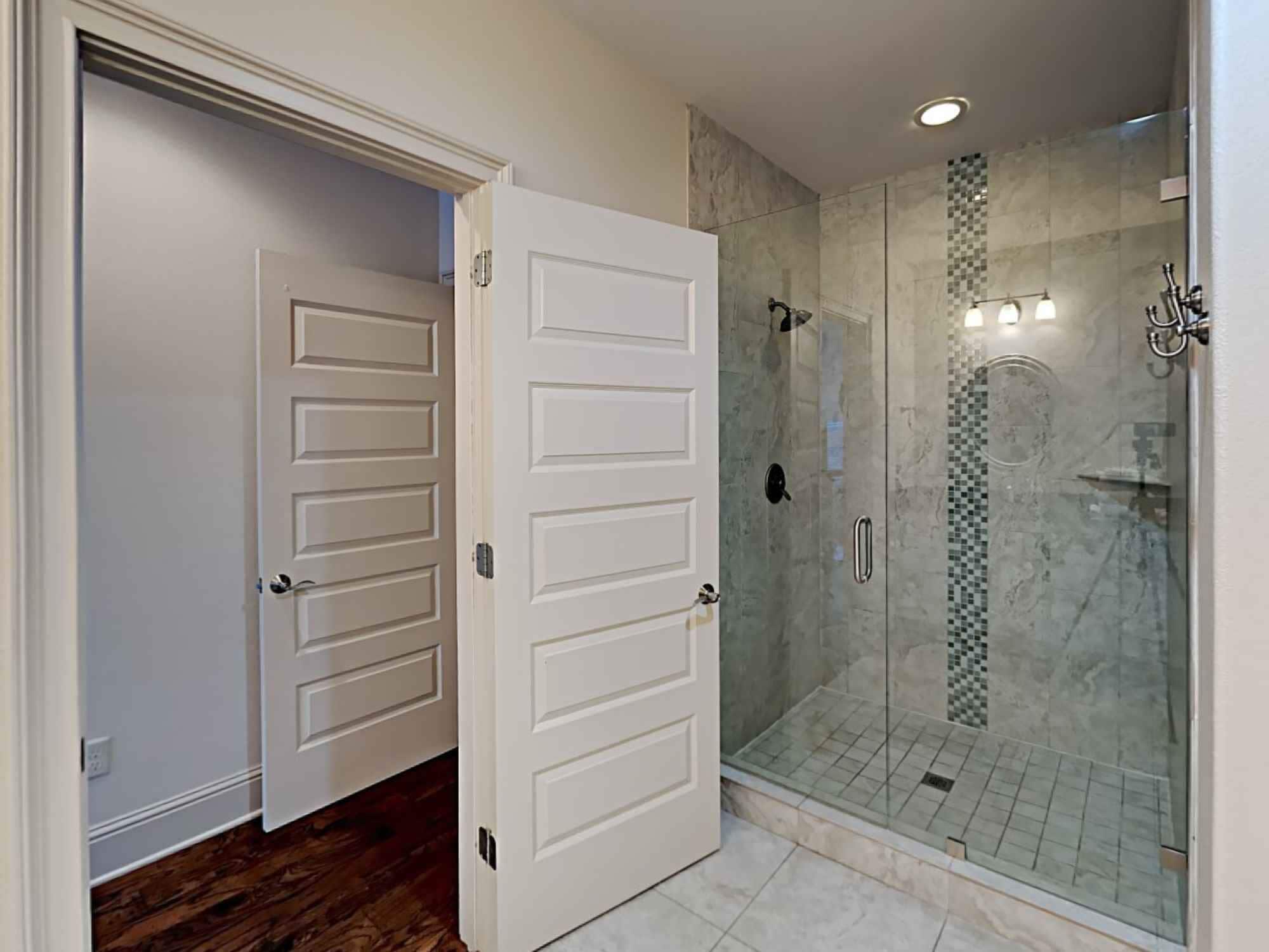 Un baño moderno con cabina de ducha de vidrio, puertas blancas y suelo de baldosas.